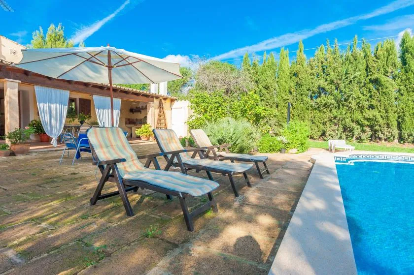 A sunny poolside patio with lounge seating and a large shade umbrella.