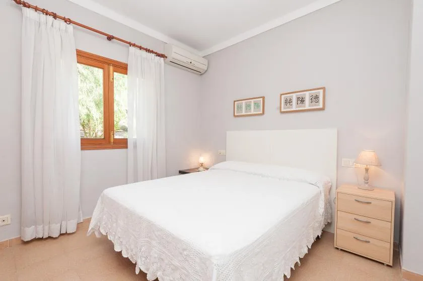 A bright bedroom with a neatly made bed and a wooden-framed window.