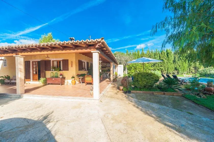 Un patio cubierto junto a un jardín, con asientos al aire libre y una sombrilla azul.