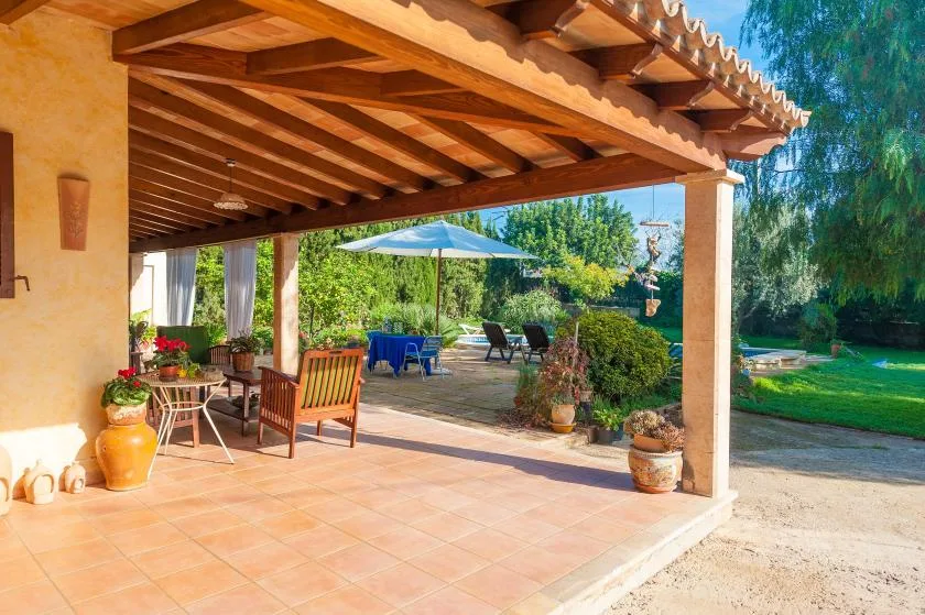 A covered patio with seating opens onto a garden with a blue umbrella.