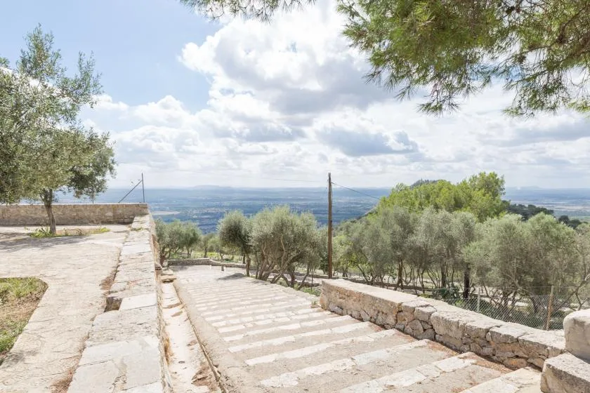 A stone terrace with steps overlooks a tree-covered landscape and distant hills.