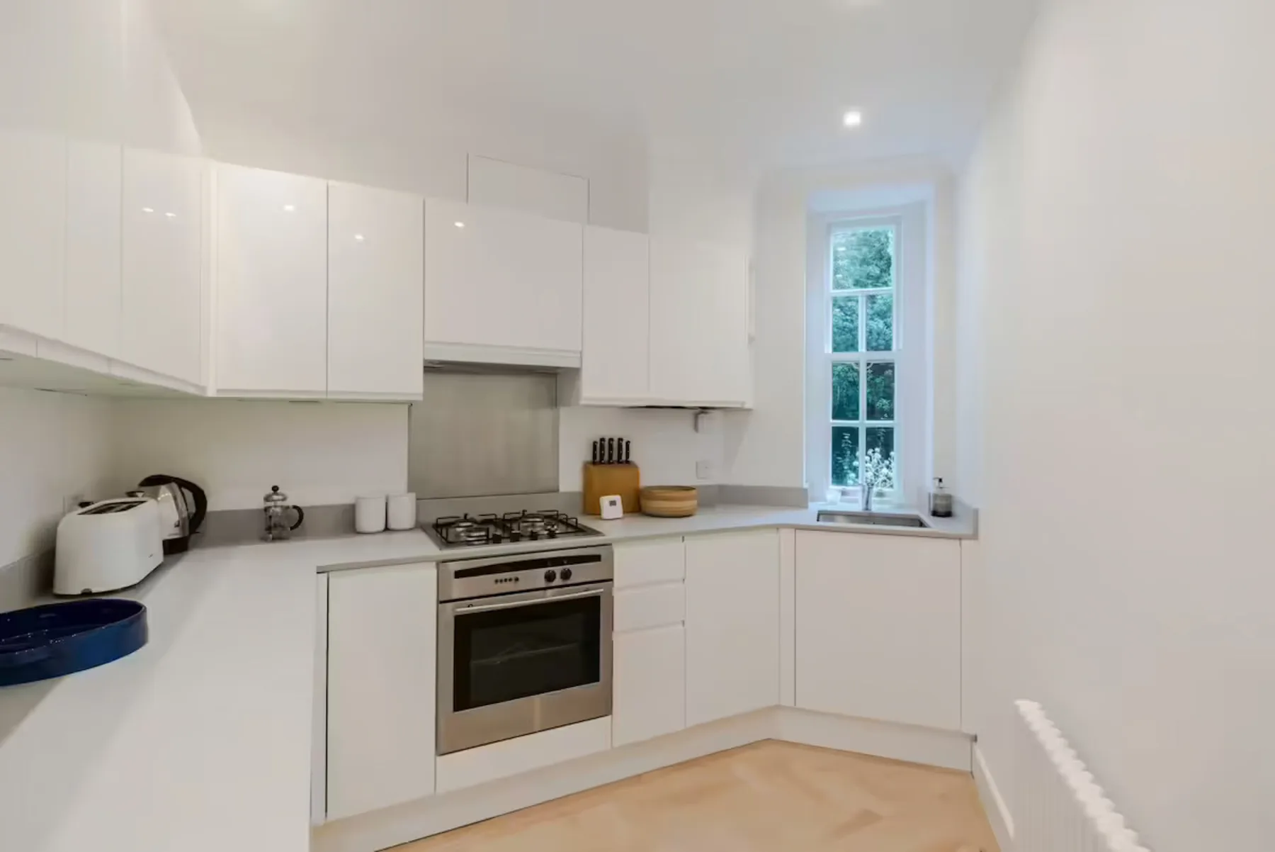 A bright kitchen with white cabinets, an oven, and a tall window.