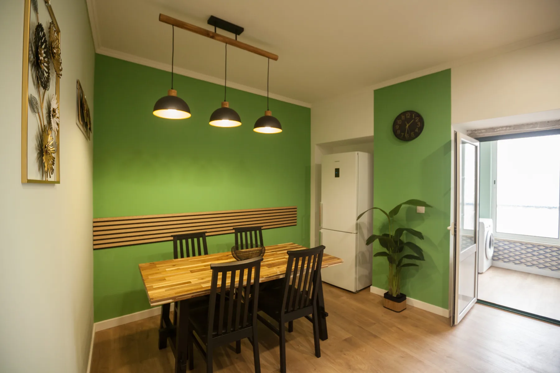A dining area with a wooden table and black chairs beside a green wall.