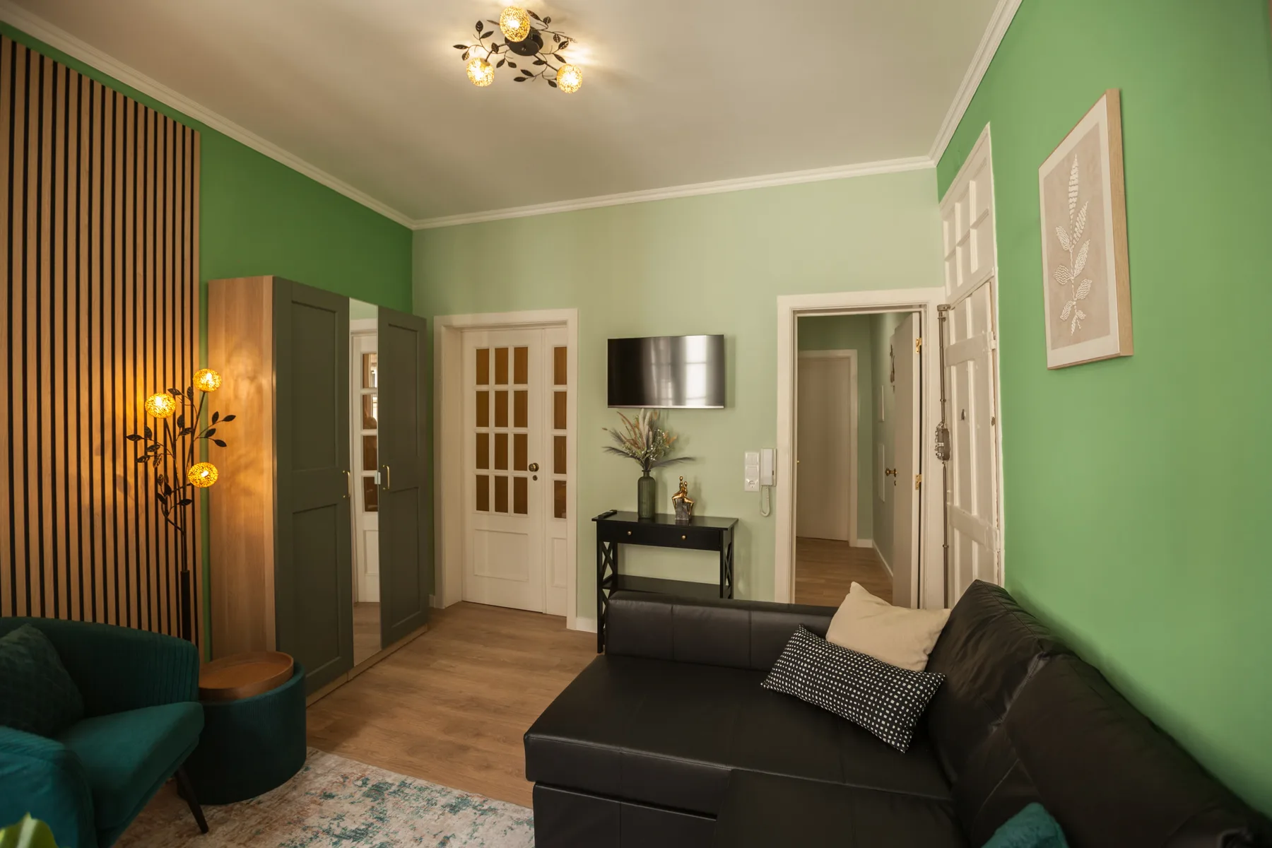 A living room with green walls, dark seating, and a wall-mounted television.