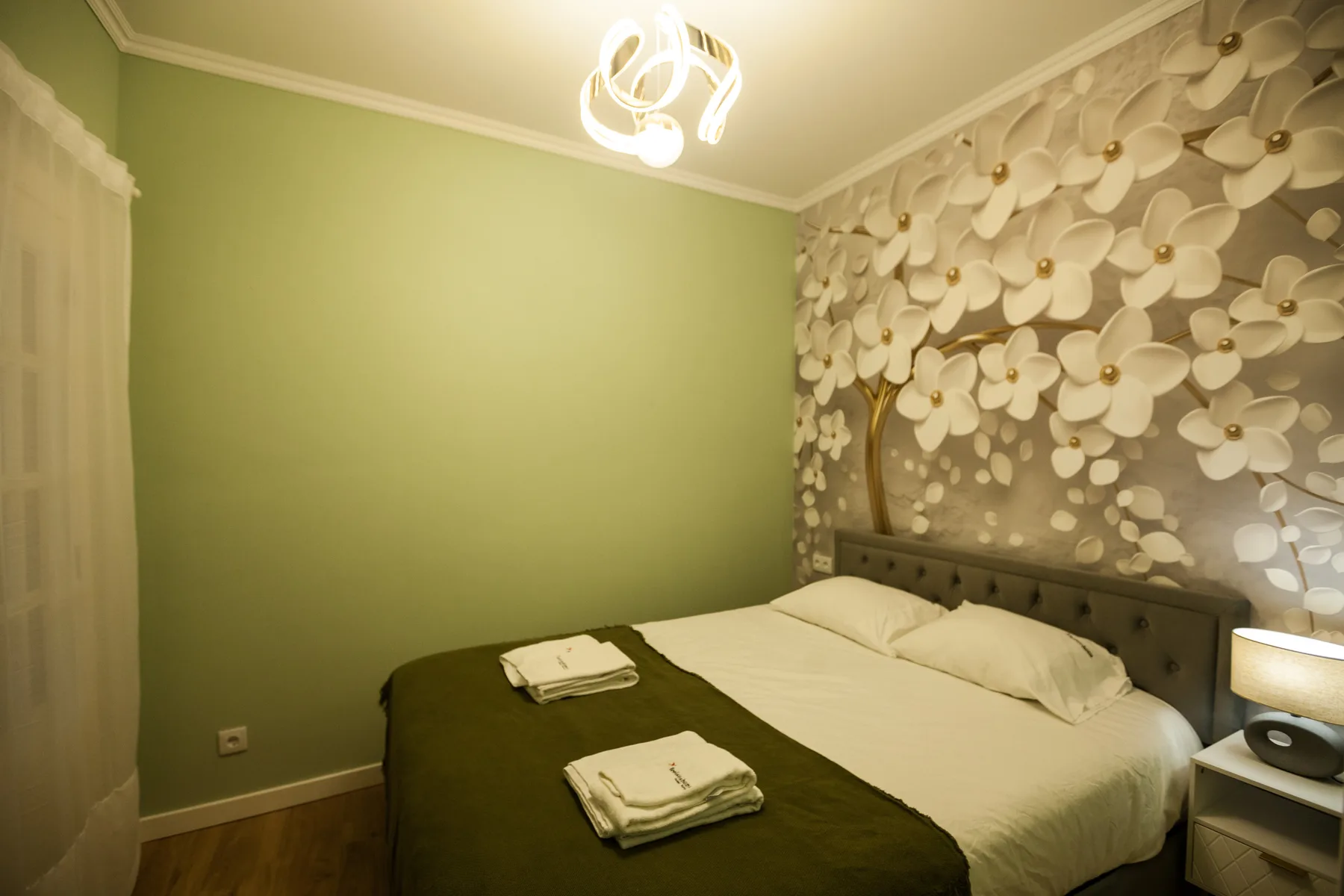 A bedroom with a bed, folded towels, and floral-patterned wallpaper.