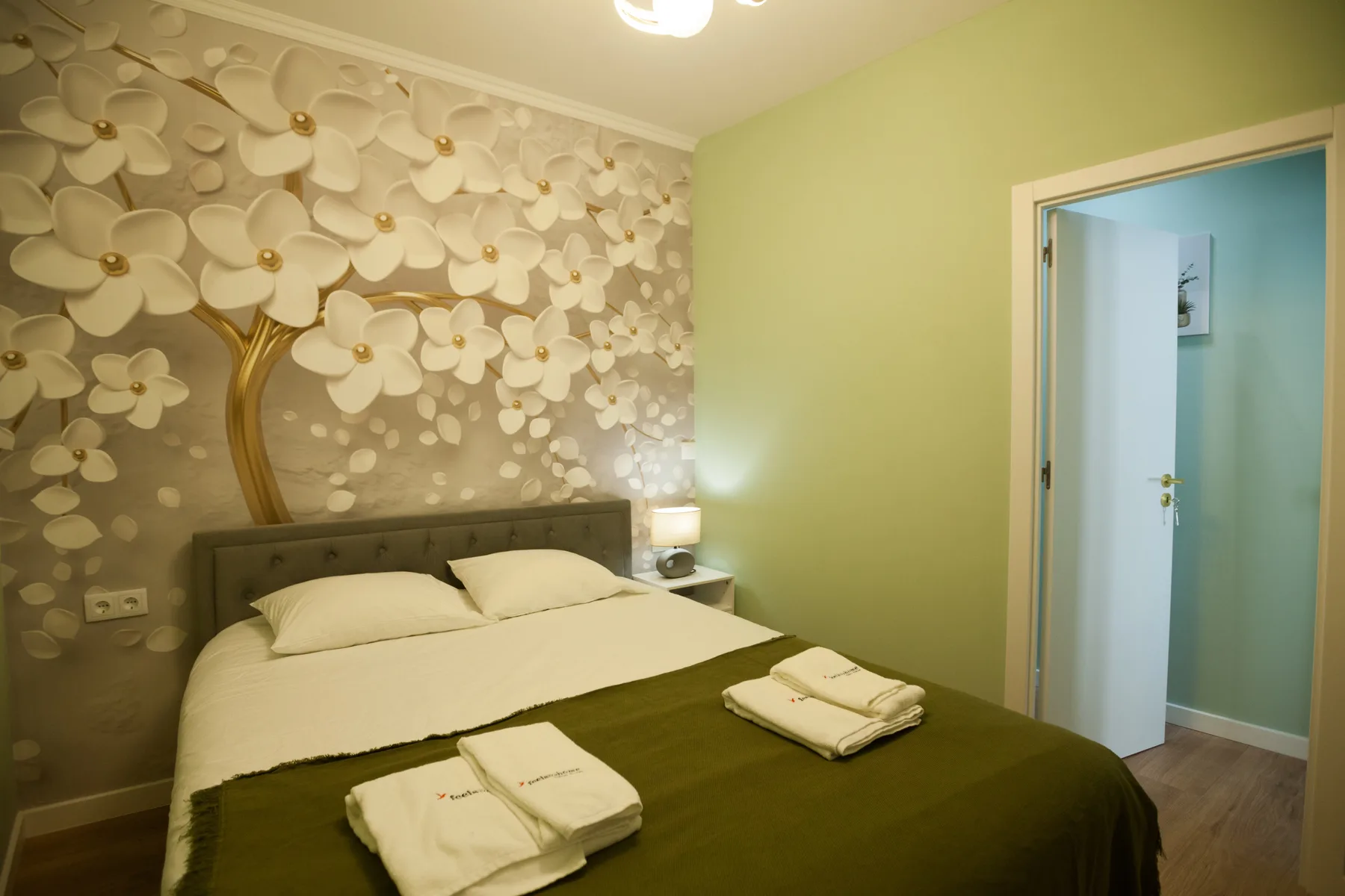 A bedroom with a neatly made bed and a decorative floral wall.