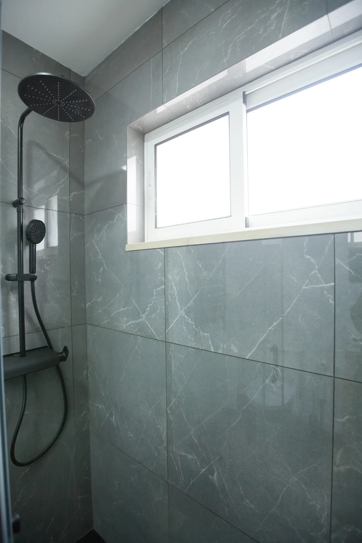 A tiled shower area with a handheld showerhead and a bright window.