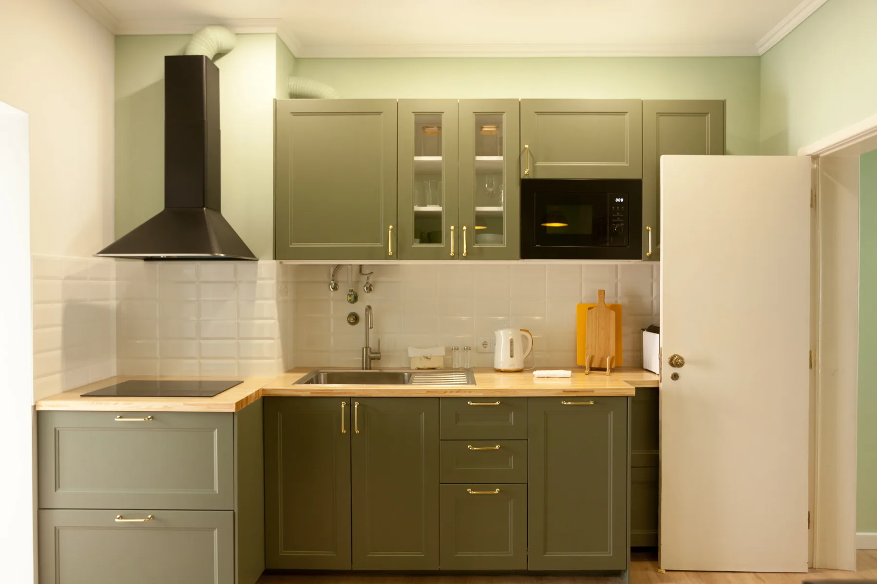 A compact kitchen with green cabinets, a countertop, and built-in appliances.