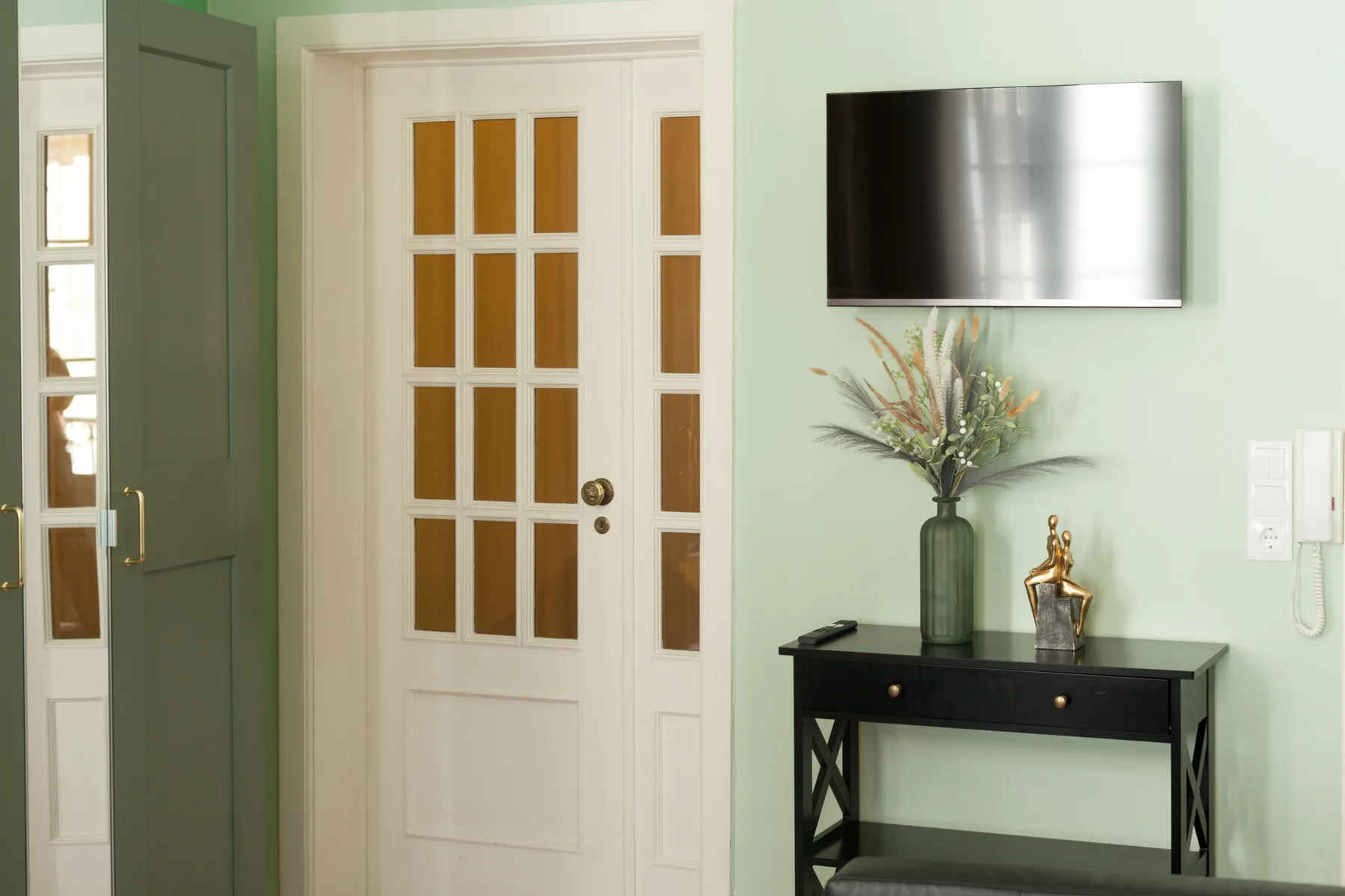 An interior entryway with a white paneled door and a console table beneath a television.