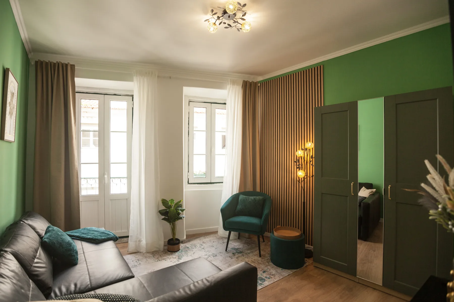 A green-walled living room with seating, windows, and a wood floor.