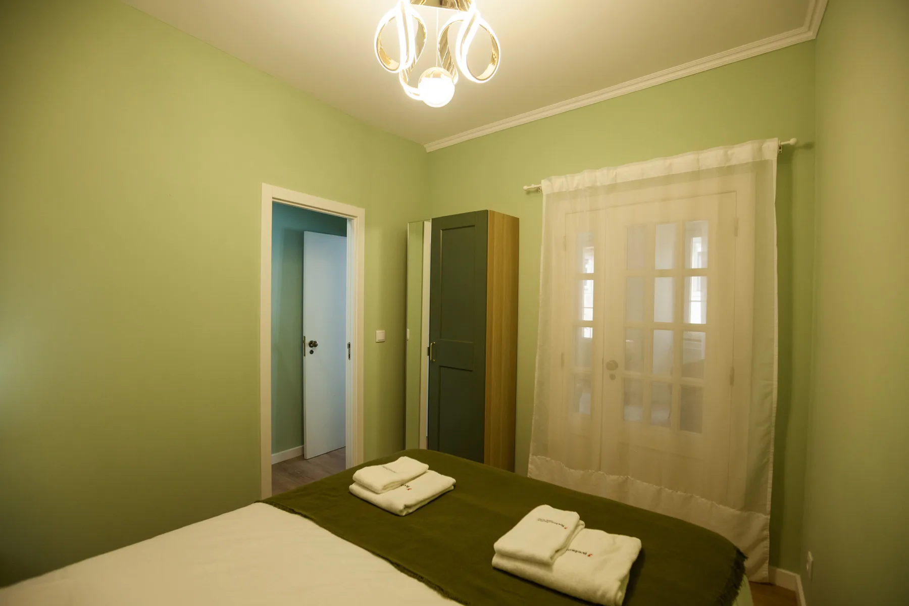 A bedroom with a bed, folded towels, and a curtained window.