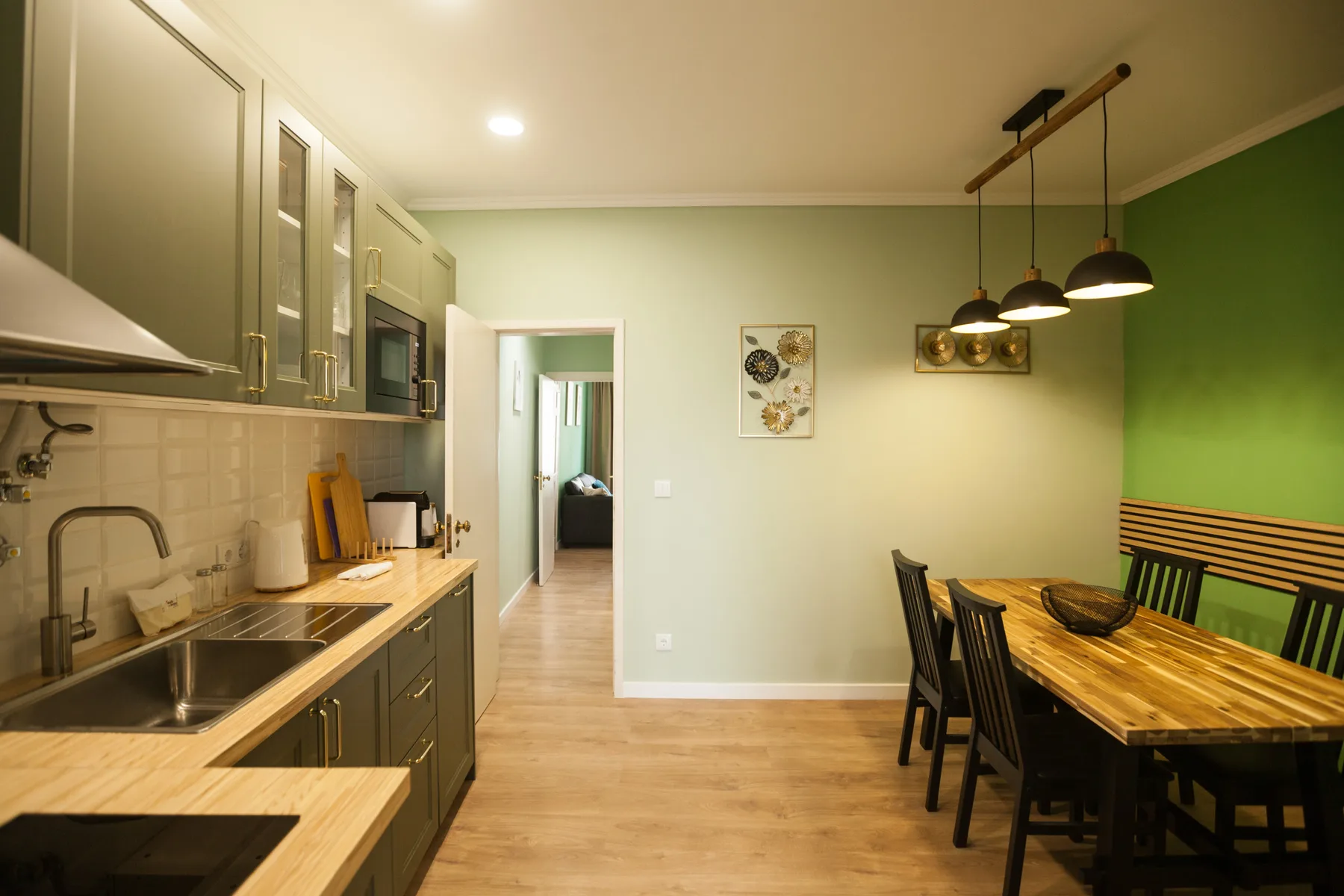 A kitchen and dining area with a wooden table and pendant lights.