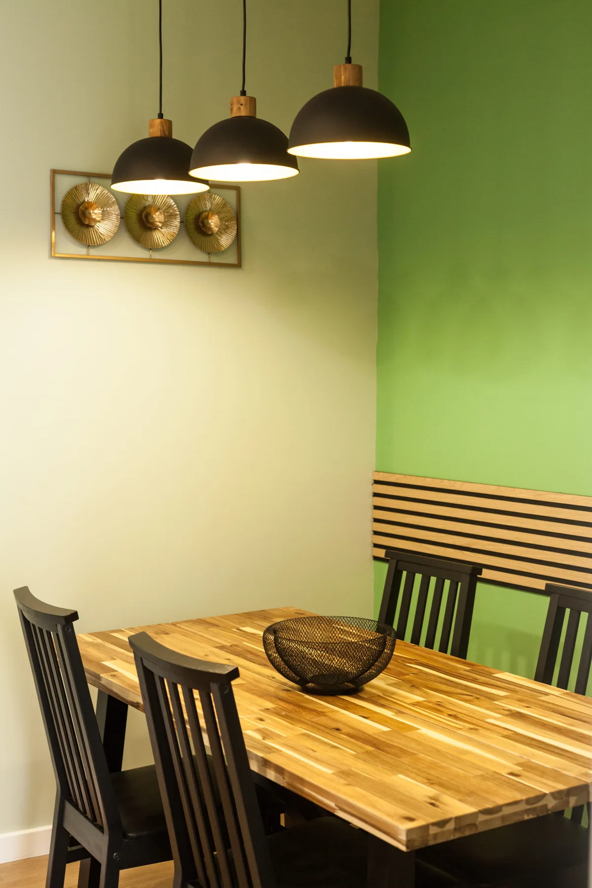 A dining area with a wooden table, dark seating, and pendant lights.