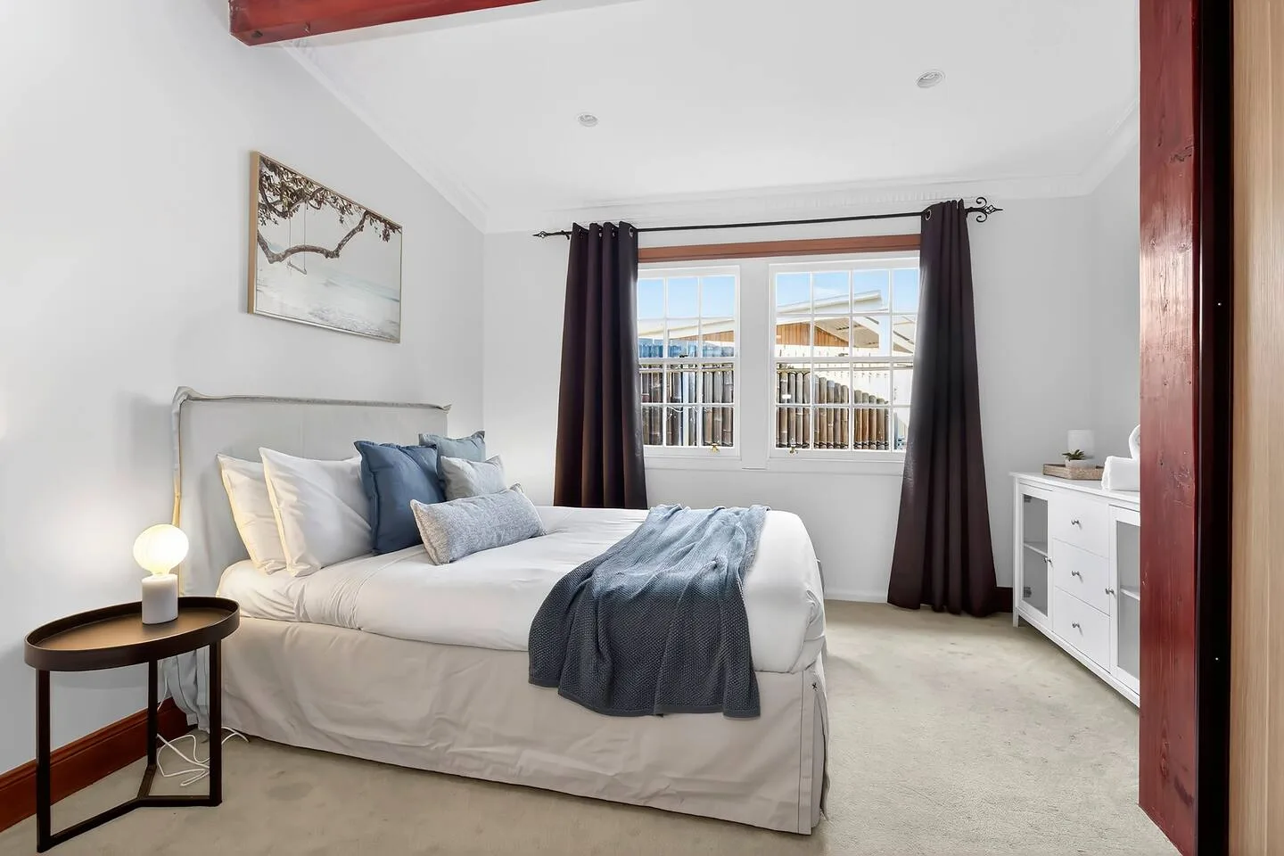 Un dormitorio luminoso con una cama, cortinas oscuras y una cómoda blanca.