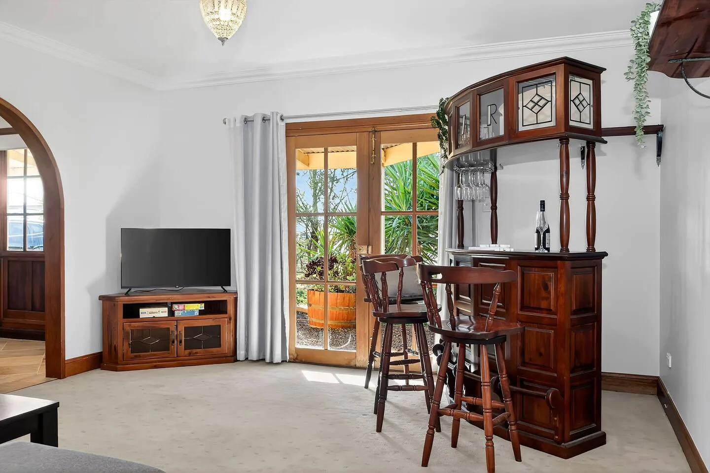 Una sala de estar tiene una barra de madera con taburetes junto a puertas acristaladas que dan a la vegetación.