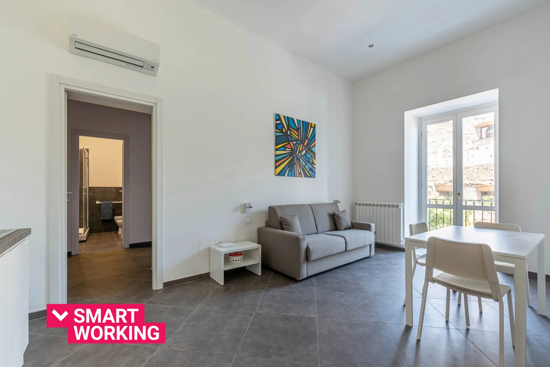 A bright living room with seating and a dining table beside large windows.