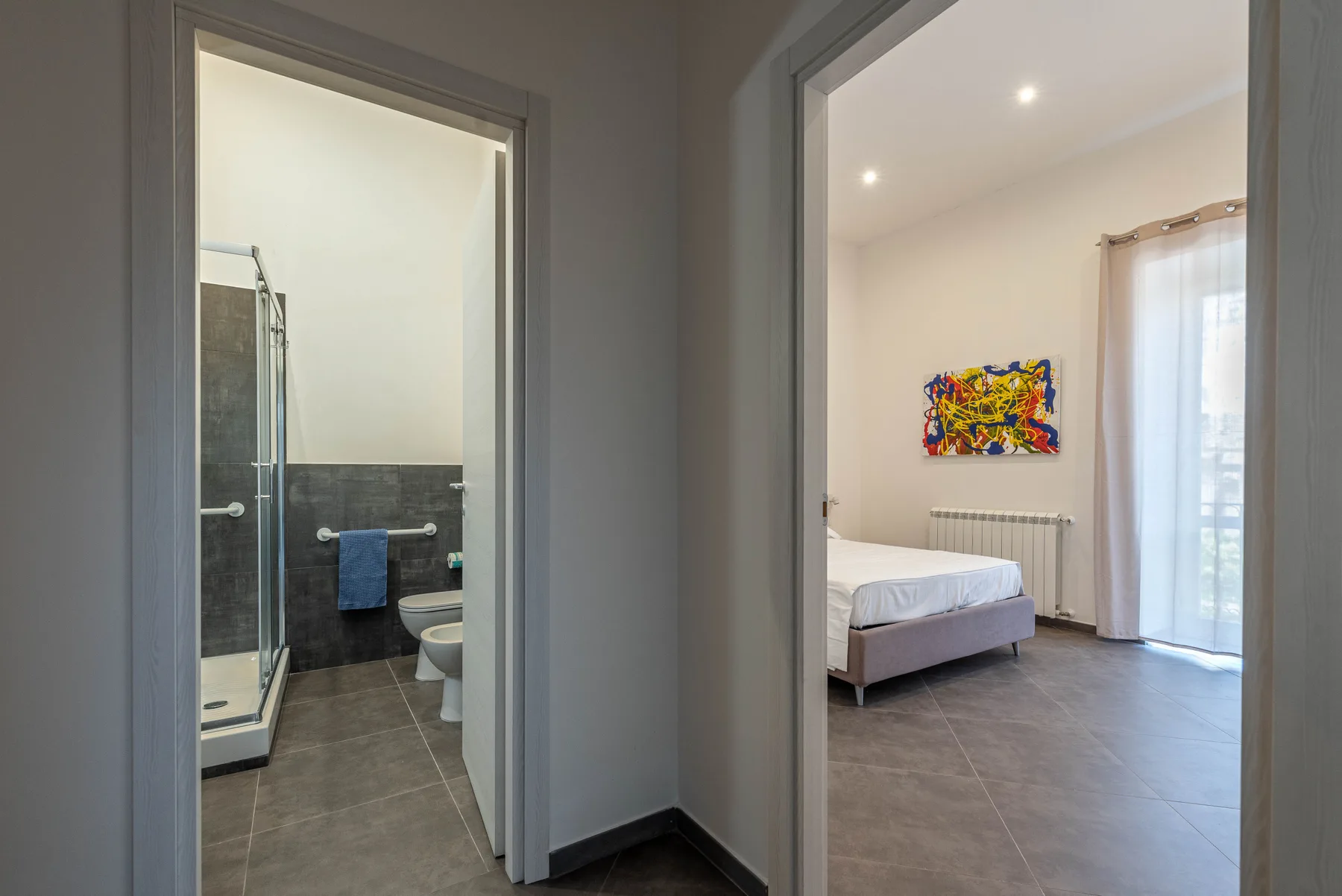 A hallway opens onto a bathroom and a bedroom with colorful wall art.
