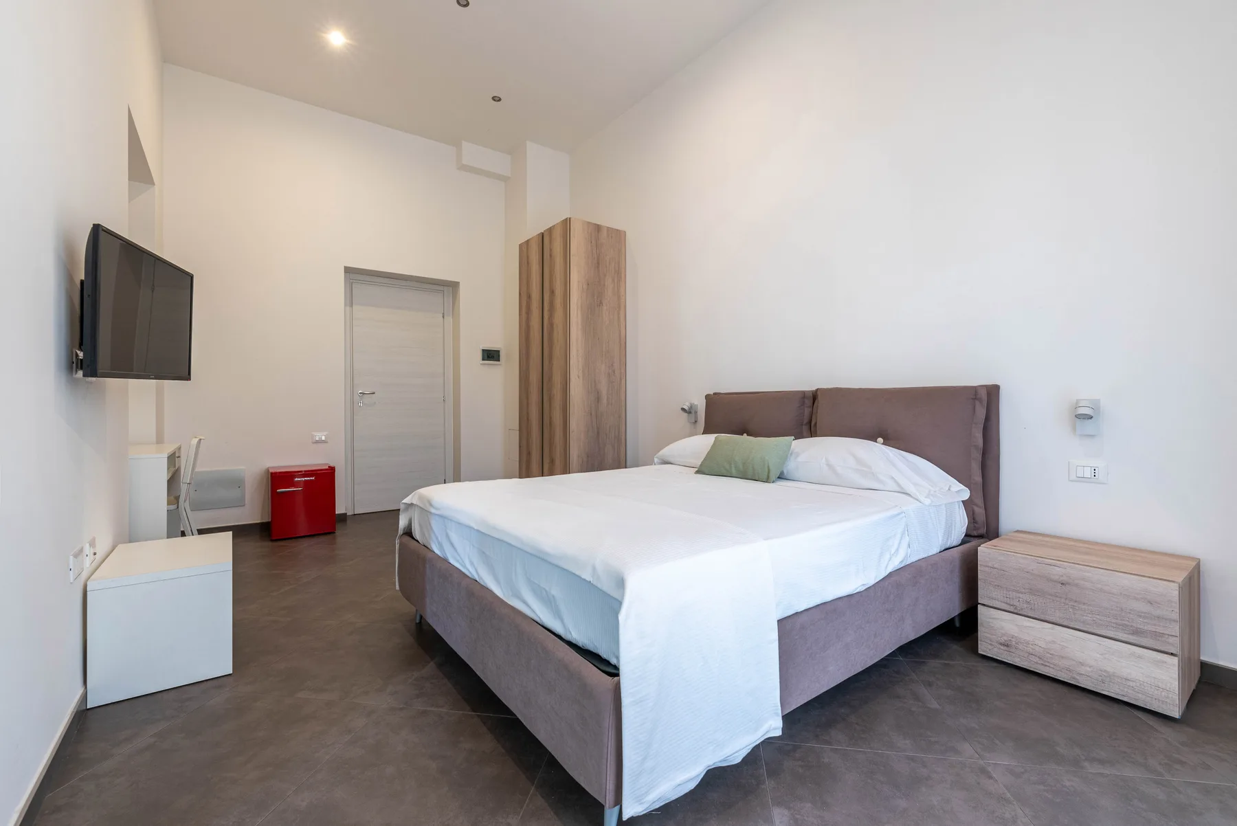 A bright bedroom with a neatly made bed and wall-mounted television.