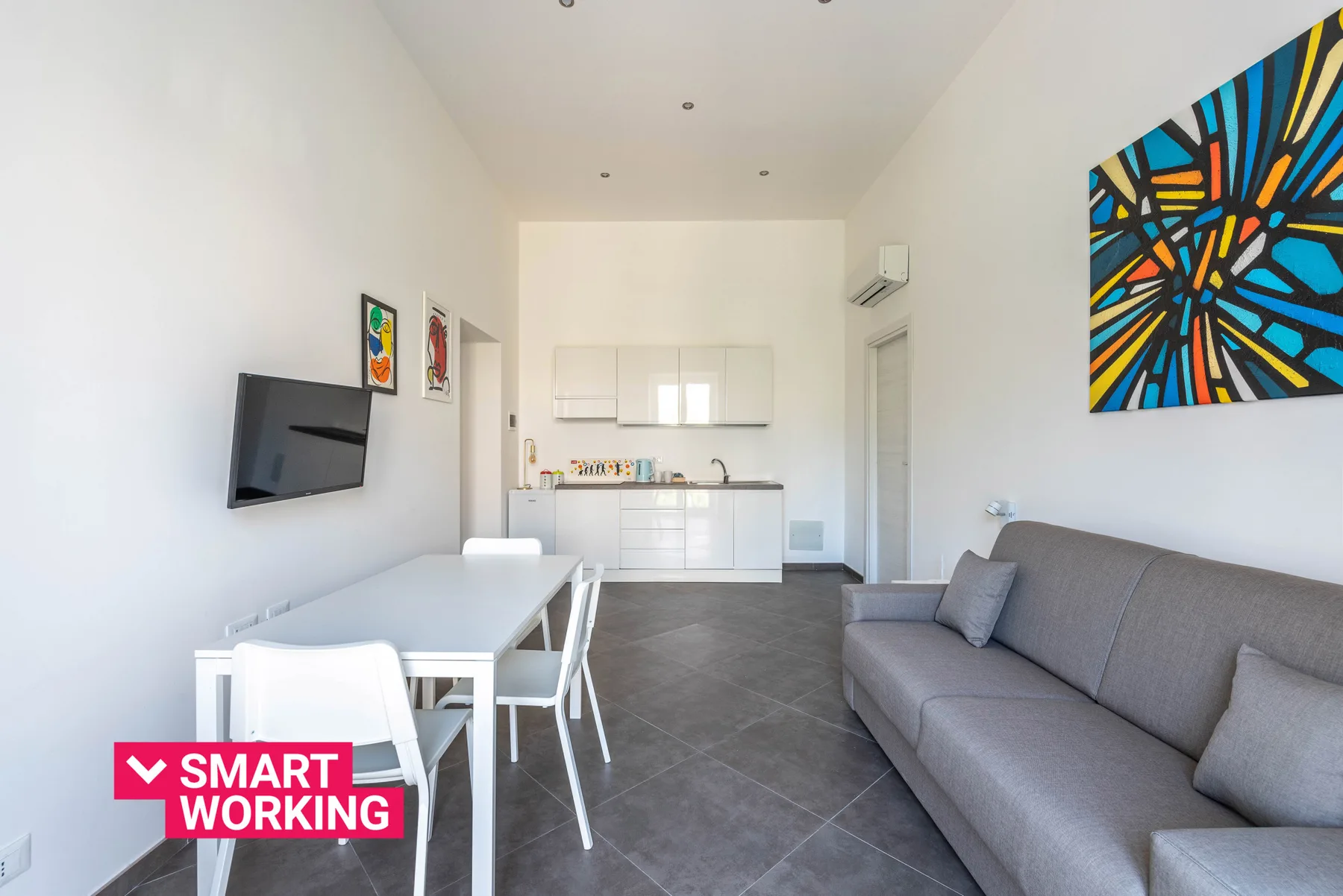 A bright living and dining area opens onto a compact kitchen, with a gray sofa.