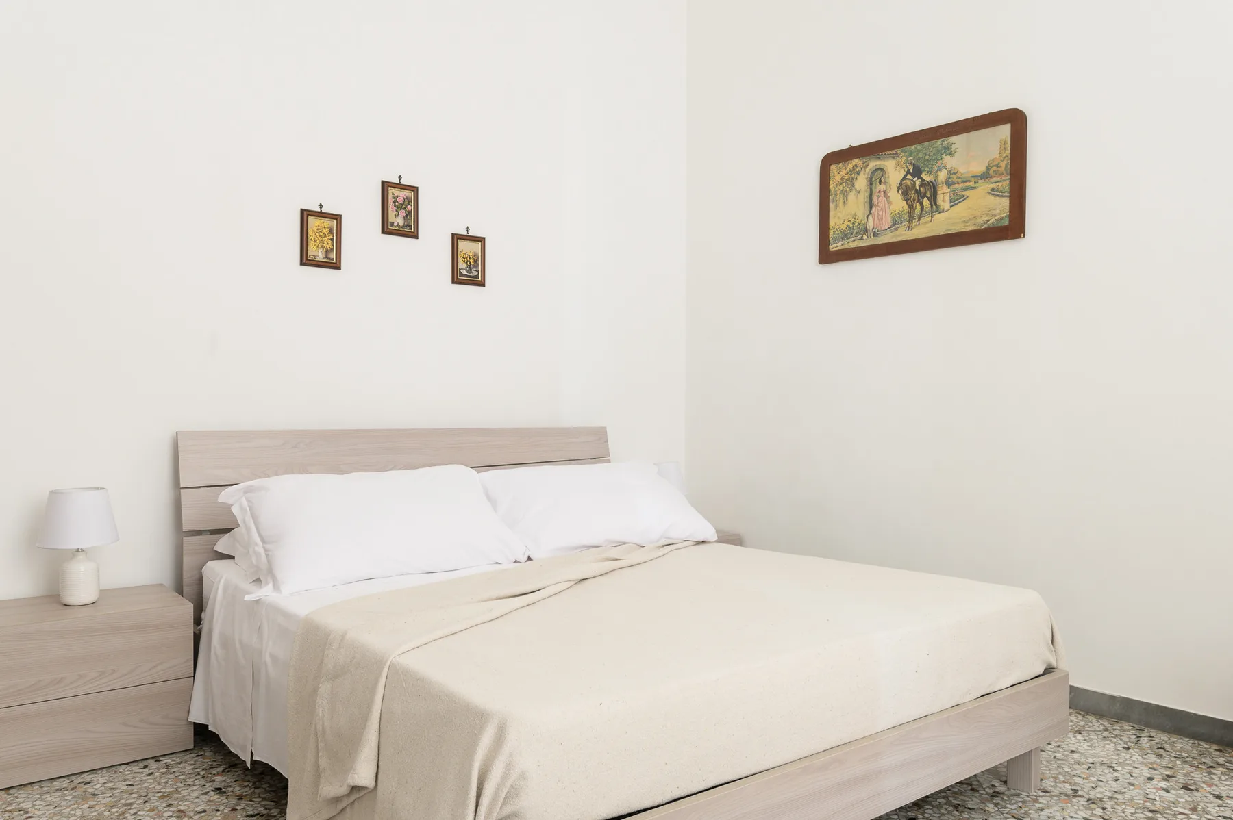 A bedroom with a neatly made bed and framed pictures on the walls.