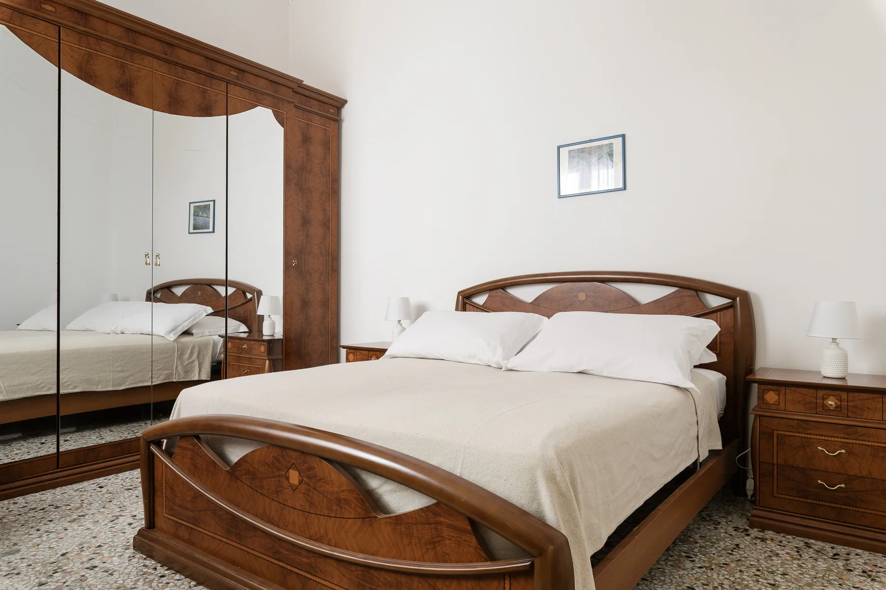 A bedroom with a wooden bed, mirrored wardrobe, and matching bedside furniture.