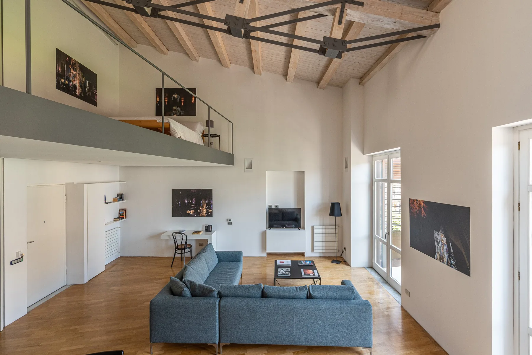 A spacious living room with blue seating beneath exposed wooden ceiling beams.