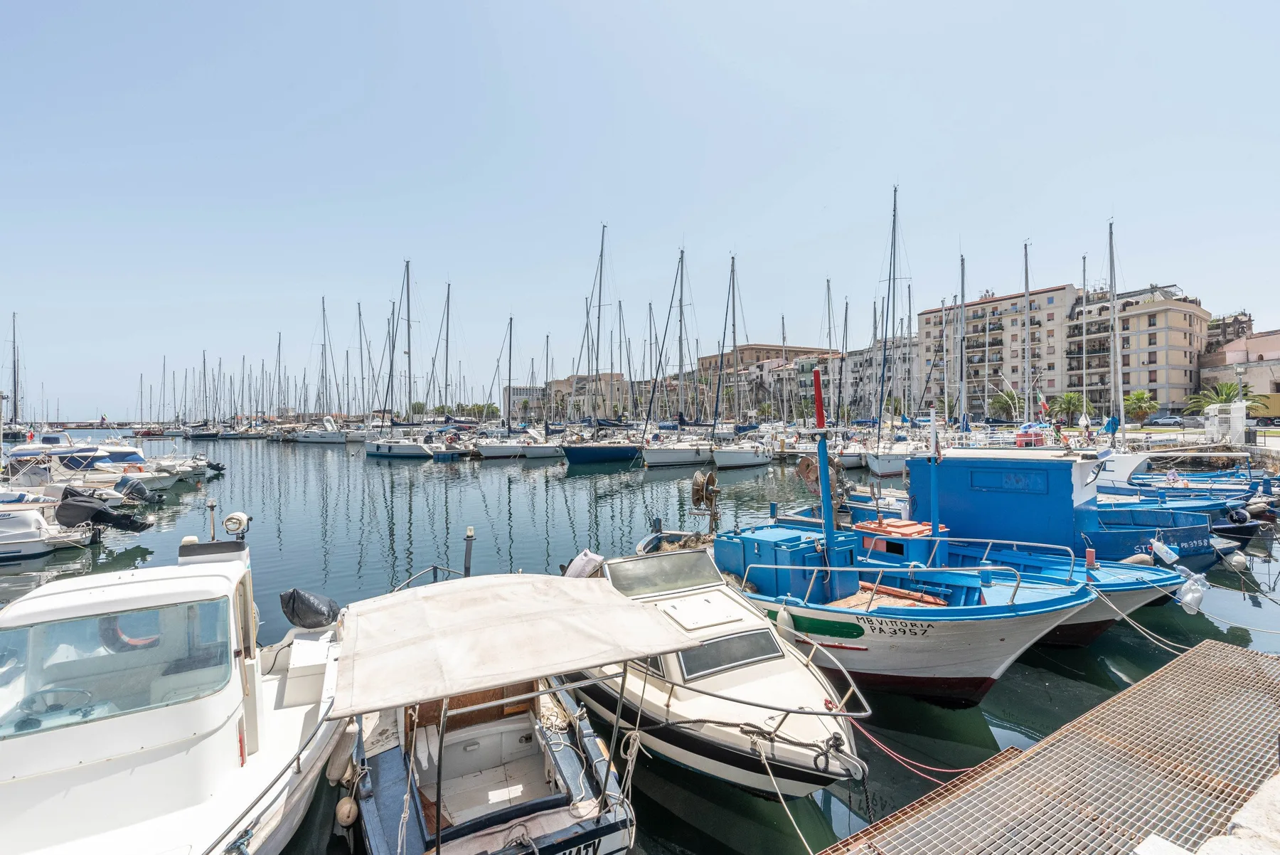 A marina filled with moored boats and sailboat masts beside waterfront buildings.