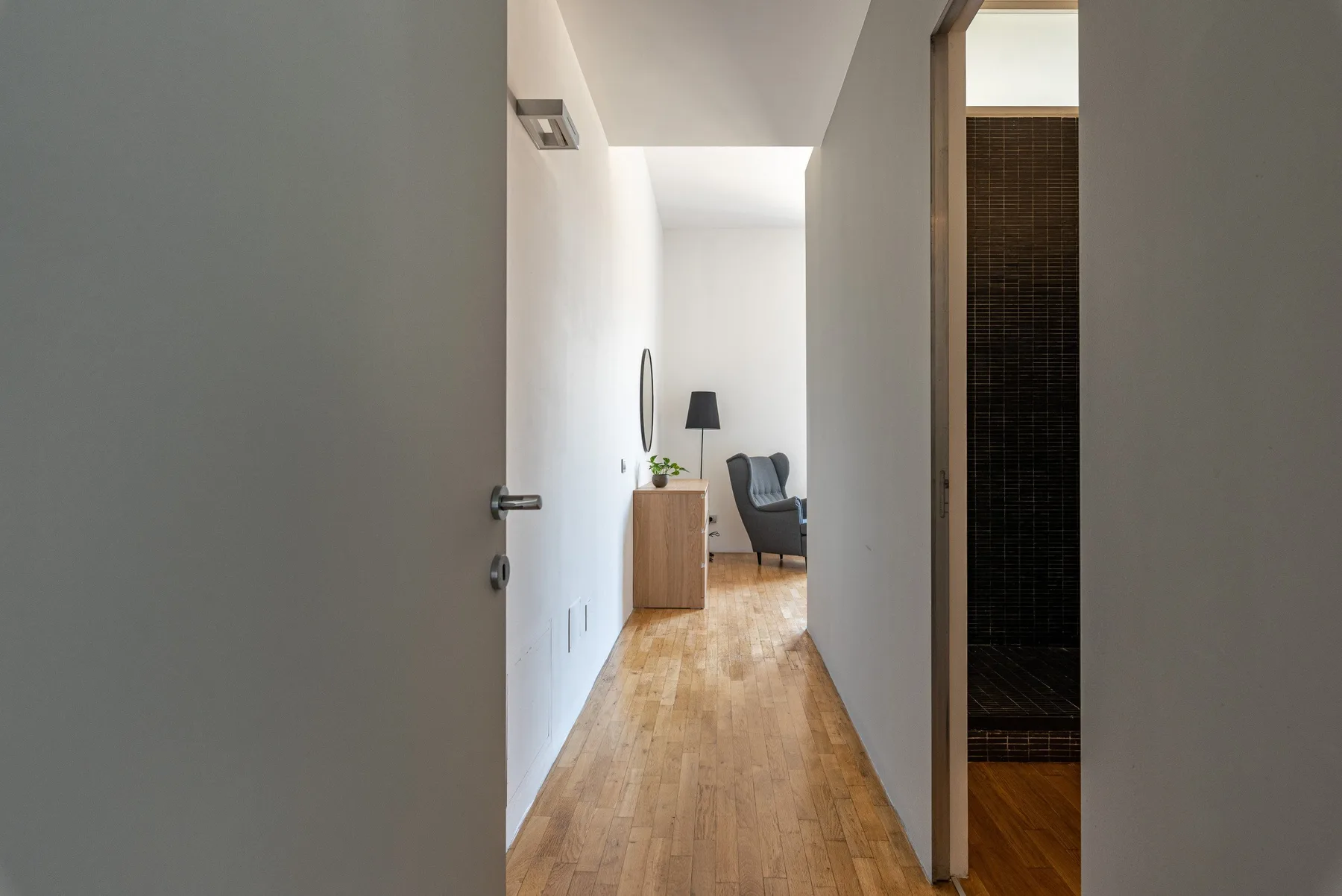 A hallway opens toward a sitting area with a chair and wooden flooring.