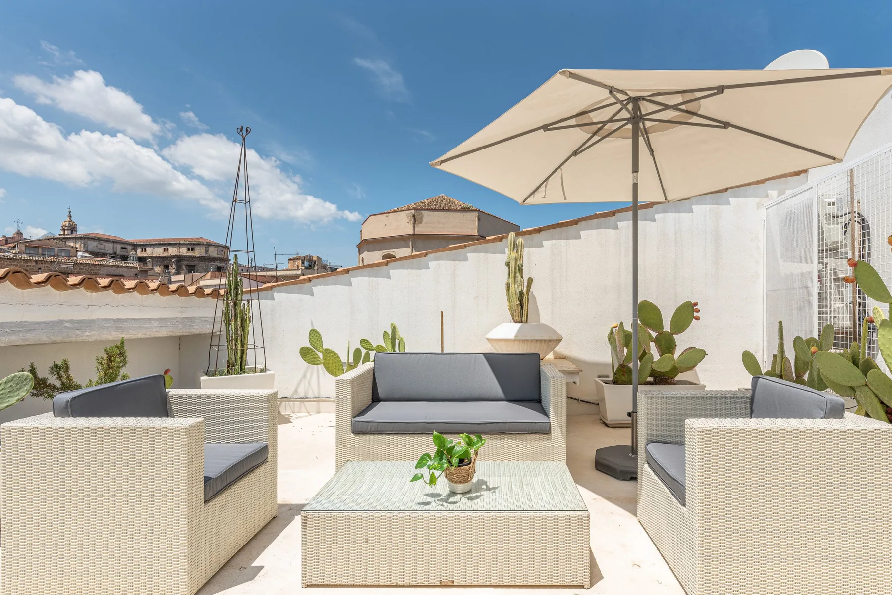 A rooftop patio seating area with a large umbrella and potted plants.