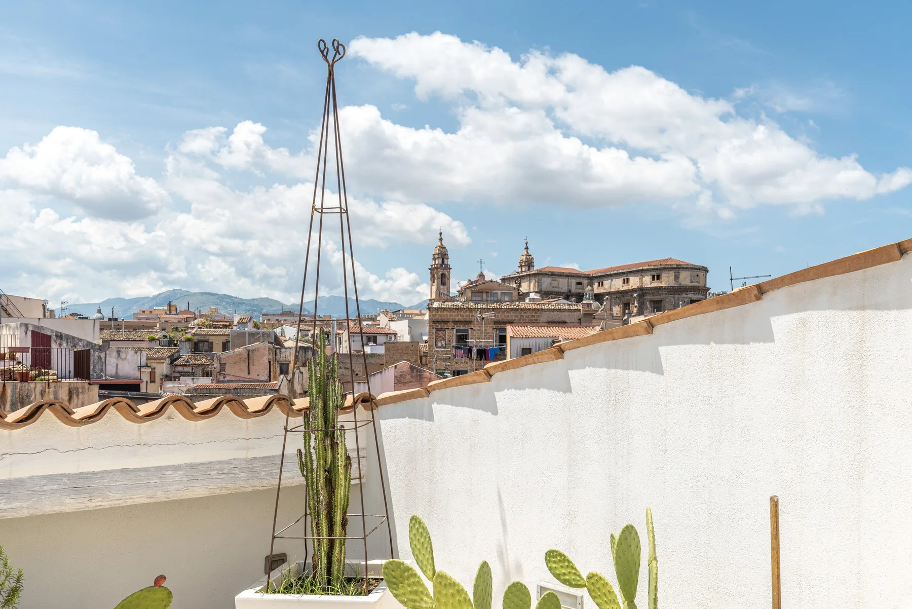 A rooftop terrace overlooks historic city buildings beneath a partly cloudy sky.