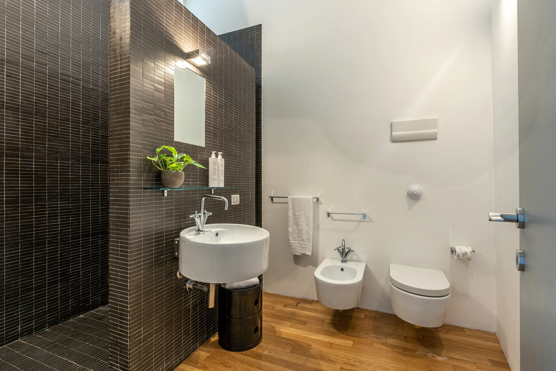 A modern bathroom with a sink, toilet, and dark tiled shower area.