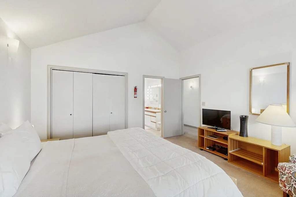 Un dormitorio luminoso con una cama grande y un televisor sobre un mueble de madera.