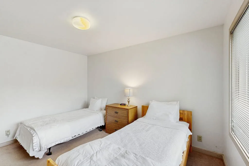 Un dormitorio luminoso con dos camas y una mesita de noche de madera.