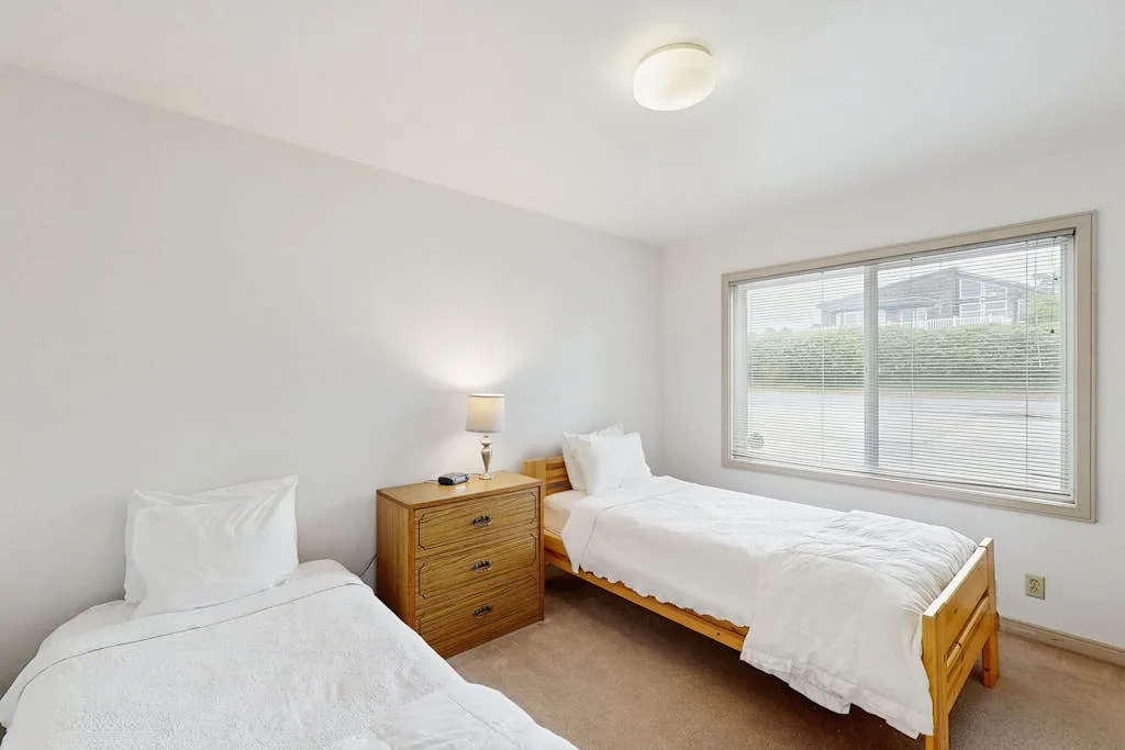 Un dormitorio luminoso con dos camas y una mesita de madera.