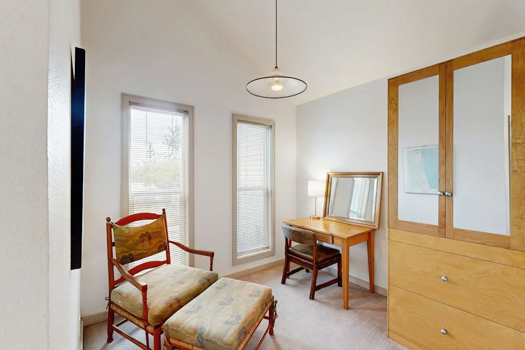 Un dormitorio luminoso con un sillón acolchado junto a un escritorio de madera.