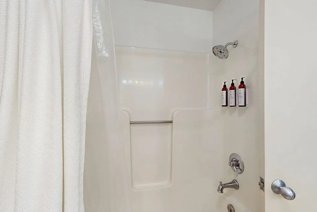 Una ducha con cortina, controles en la pared y botellas en un estante.