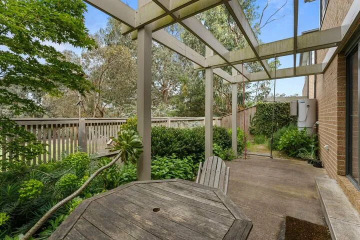 A covered outdoor patio with a wooden table and garden greenery.