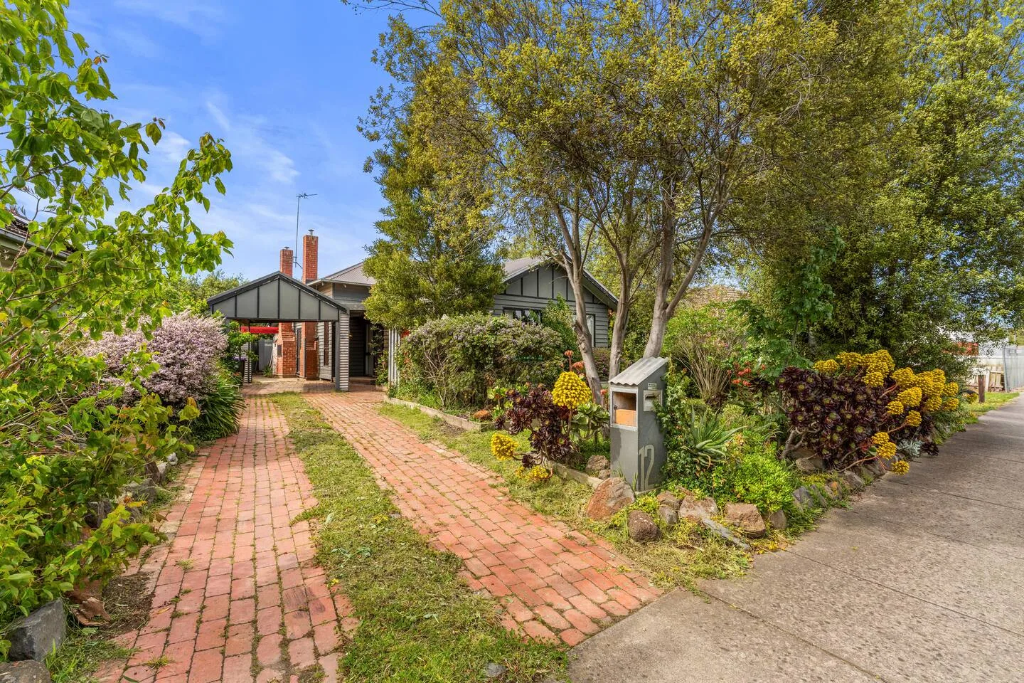 A brick path leads through a garden toward a house entrance.