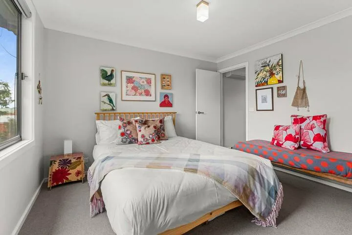 A bedroom with a neatly made bed and colorful artwork on the walls.