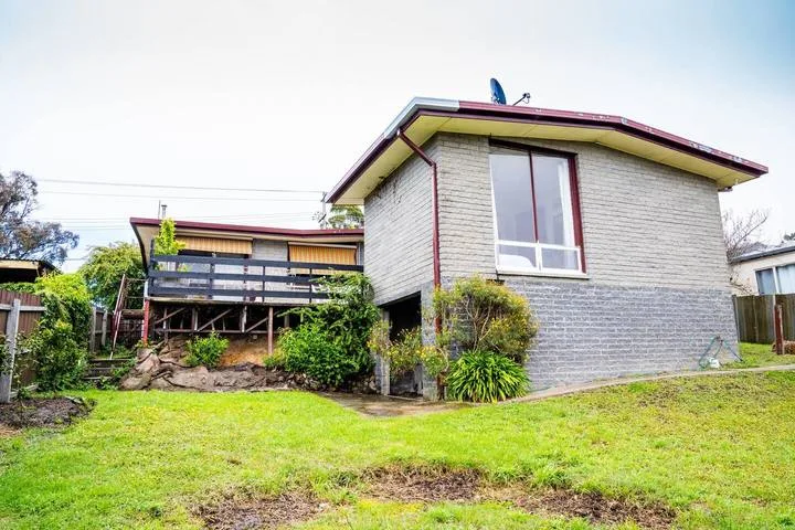 A gray house stands beside a raised wooden deck and a grassy yard.