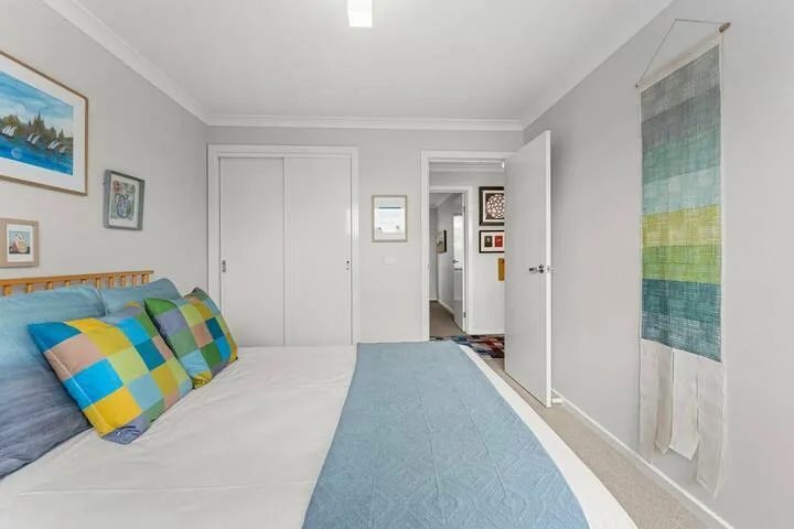 A bedroom with a bed, colorful pillows, and a blue runner.