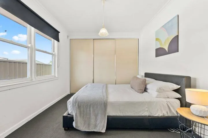 A bright bedroom with a neatly made bed beside a large window.