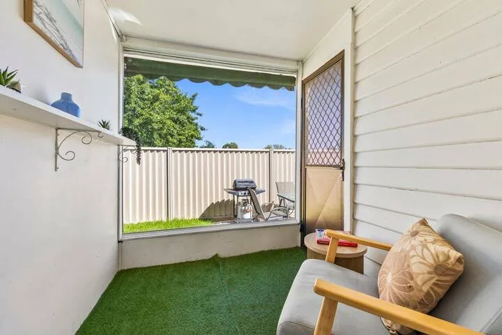 A covered patio with seating overlooks a small grill and a fenced yard.