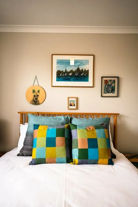 A bedroom with a neatly made bed and colorful checked pillows beneath framed artwork.