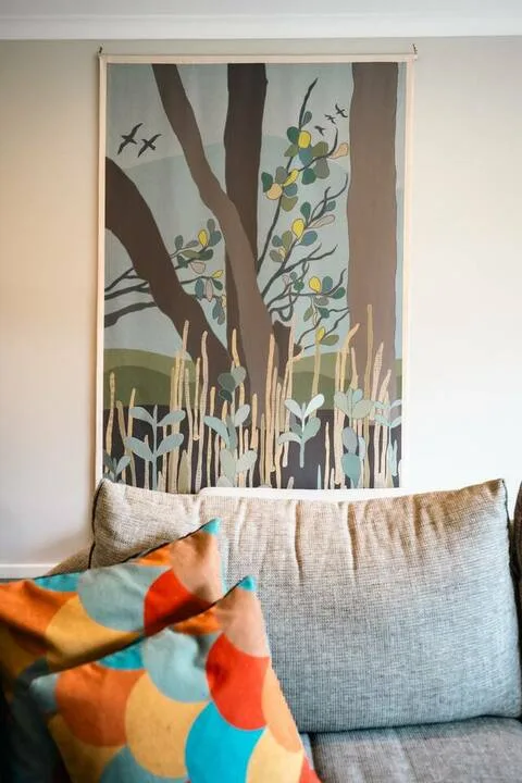 A couch with colorful cushions sits beneath a framed tree illustration.