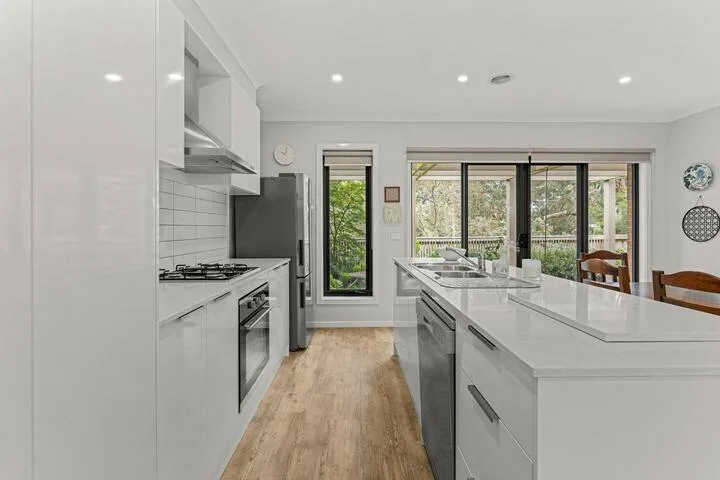 A bright modern kitchen with a long island and large windows overlooking greenery.