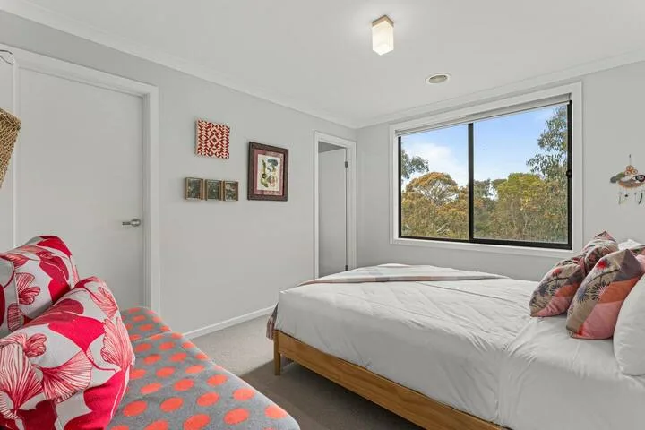 A bright bedroom with a bed beside a large window overlooking trees.