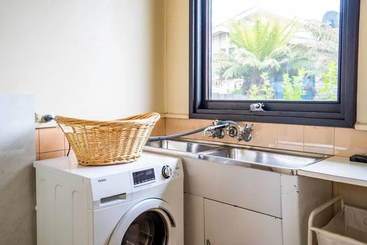 A laundry area with a washing machine beneath a window beside a sink.