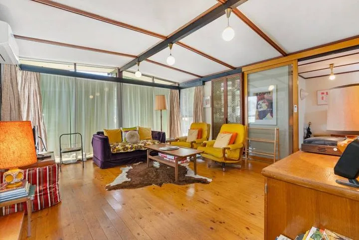 A living room with seating around a low coffee table and large curtained windows.