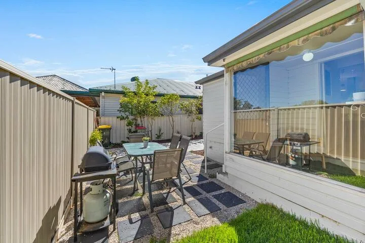 An outdoor patio has a dining table and seating beside a large window.